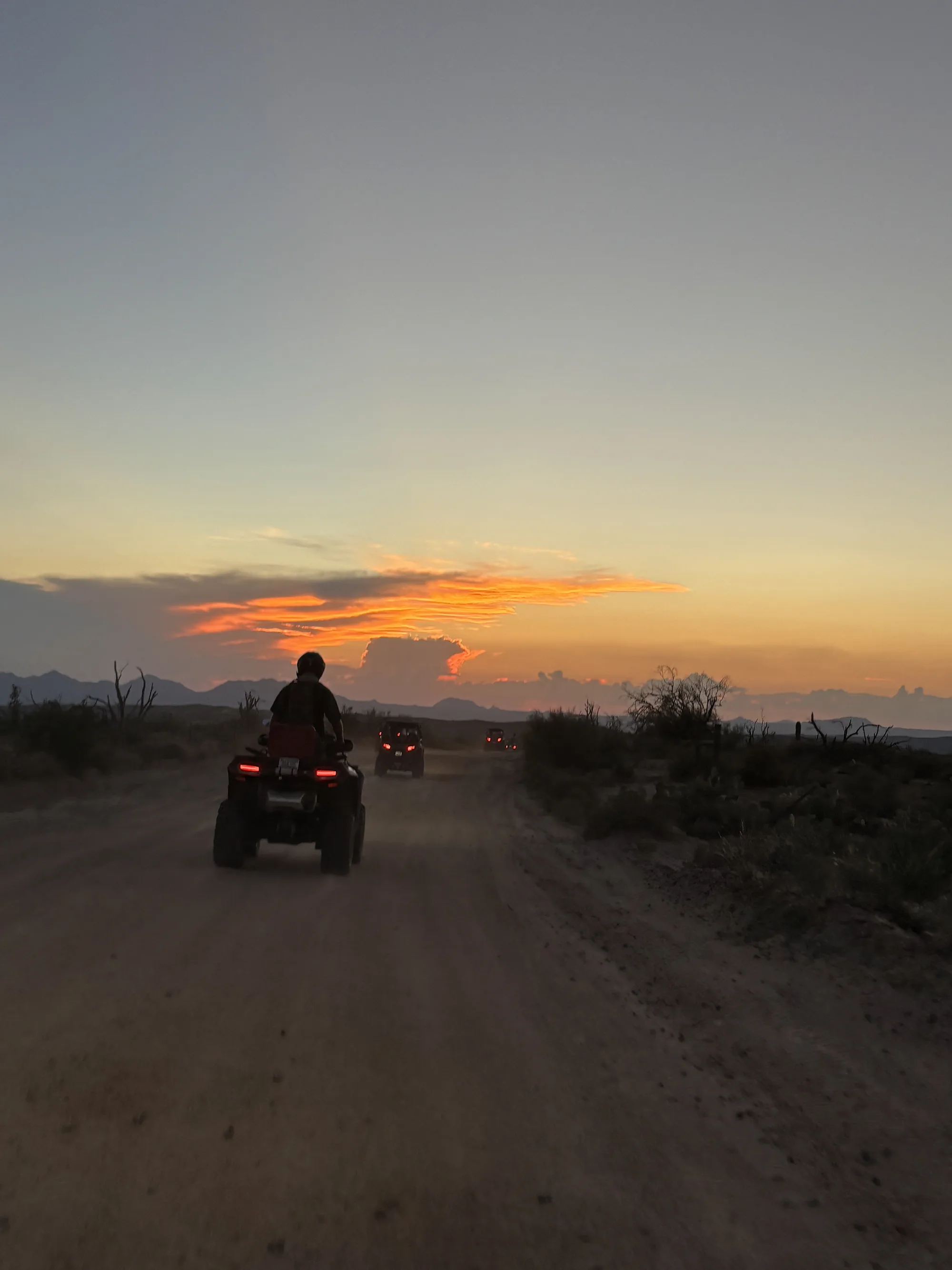 An ATV rider following the convoy down a dirt trail toward an orange sunset in the Sonoran Desert near Scottsdale