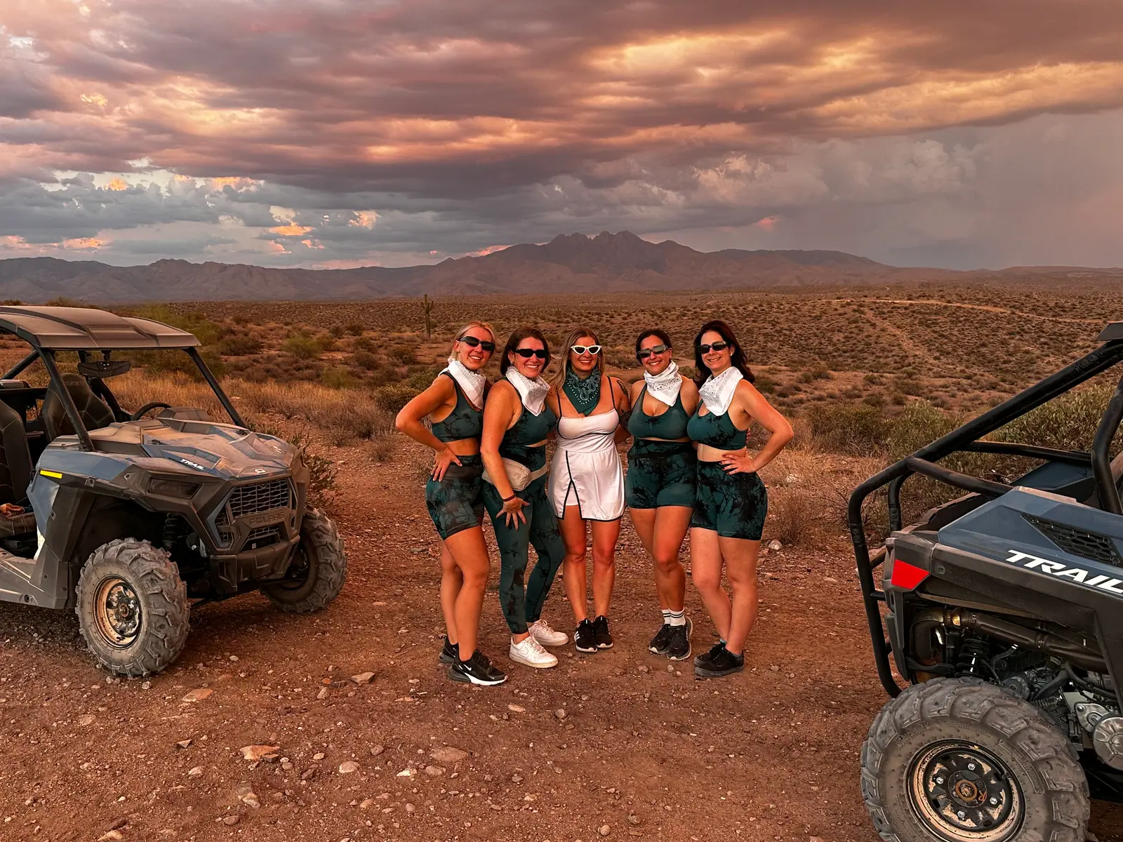 A bachelorette group in green at sunset by a Polaris buggy