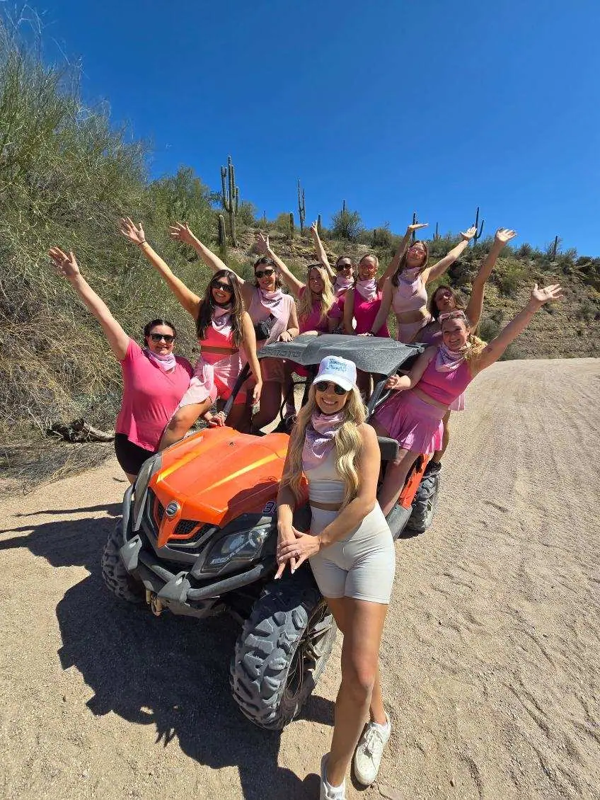 A bachelorette group in pink celebrating by an orange sand buggy