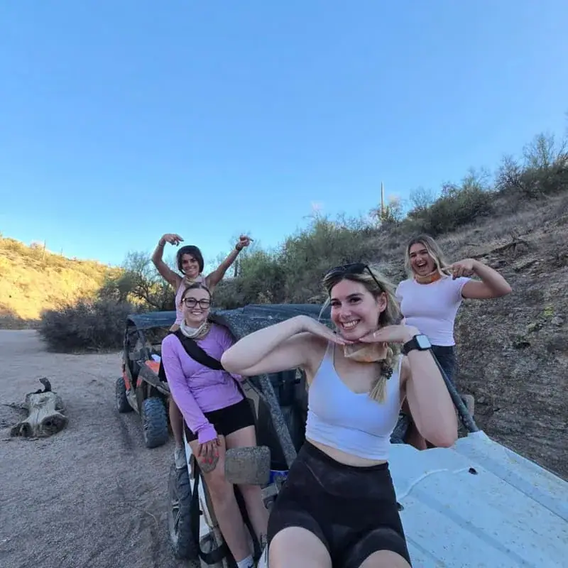 Friends posing joyfully on an ATV during a desert sunset