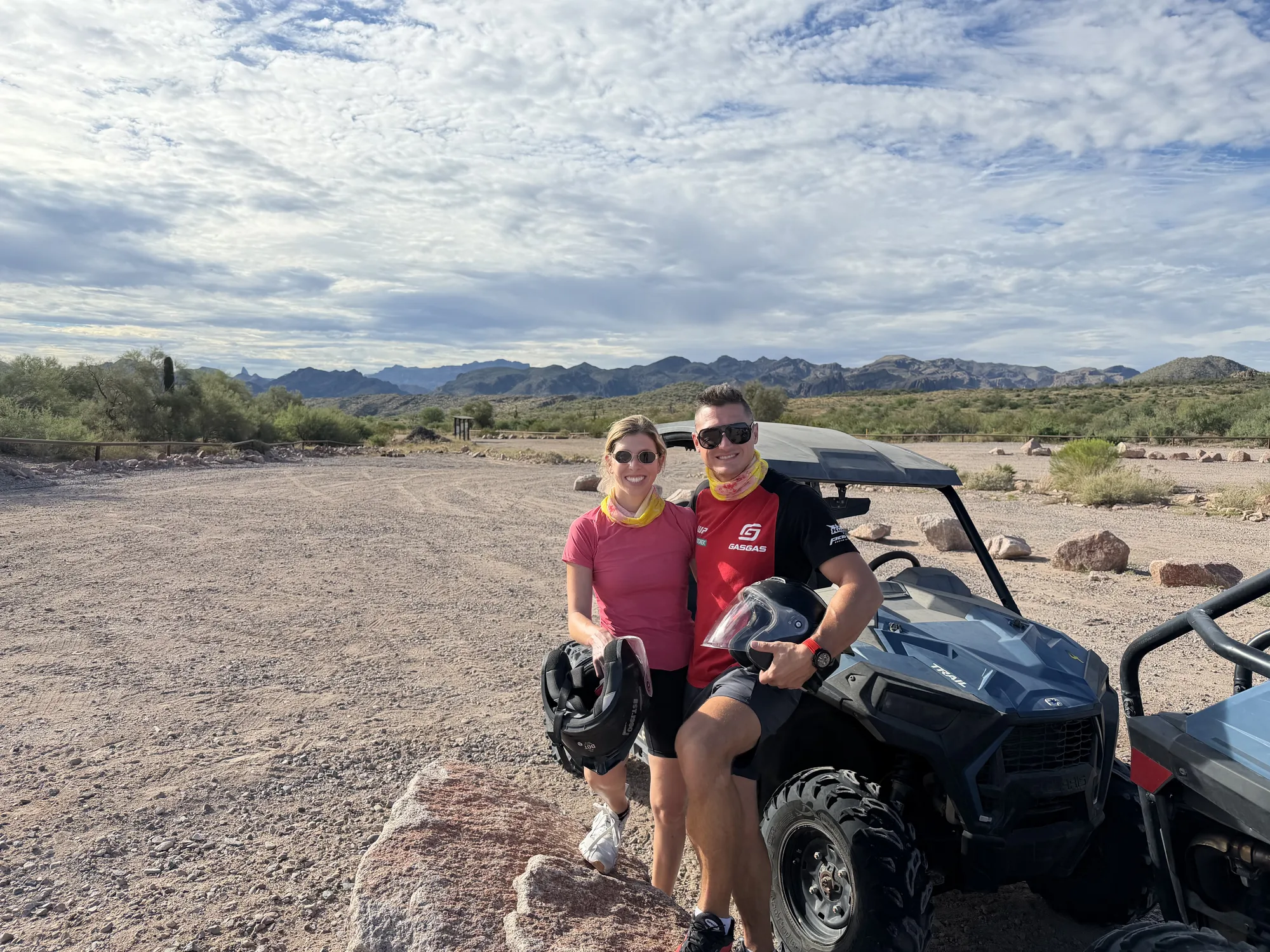 A couple holding their helmets beside a Polaris RZR Trail with desert mountains behind them before a Scottsdale UTV tour