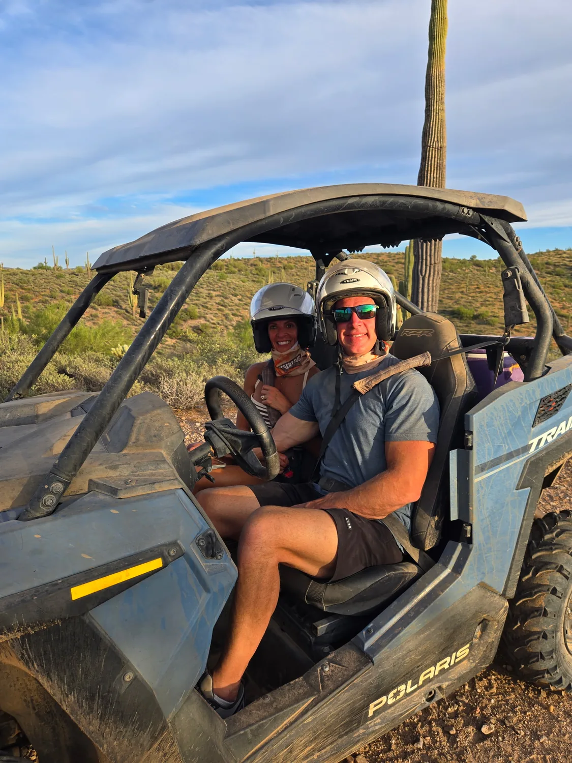 A couple seated in a Polaris RZR at golden hour beside a saguaro on a Scottsdale sunset tour
