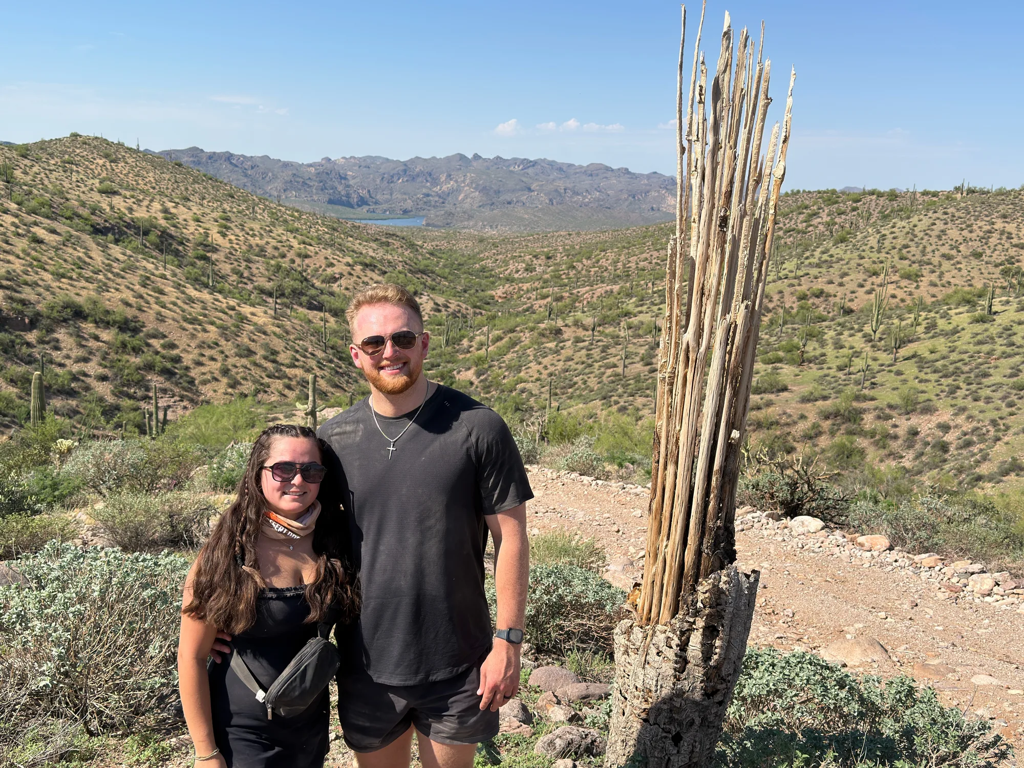 A couple on a desert trail with Saguaro Lake and mountains behind them on a Scottsdale UTV tour