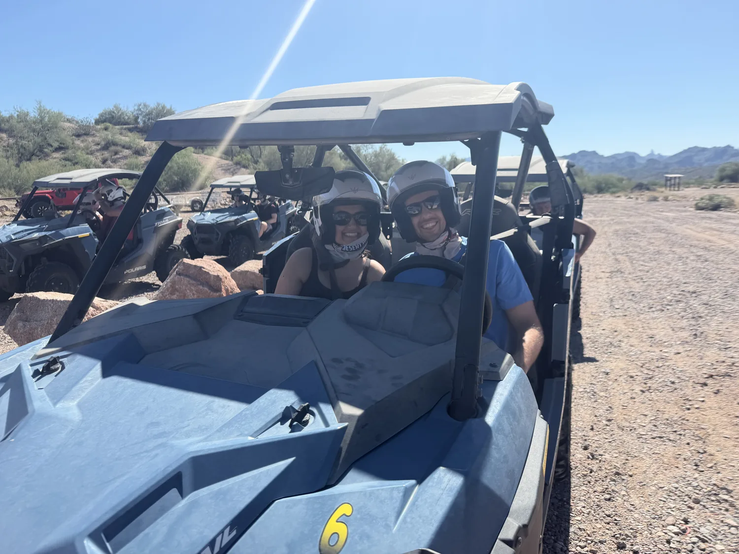 A smiling couple in the cockpit of a Polaris RZR with the tour convoy behind them on a Scottsdale desert tour