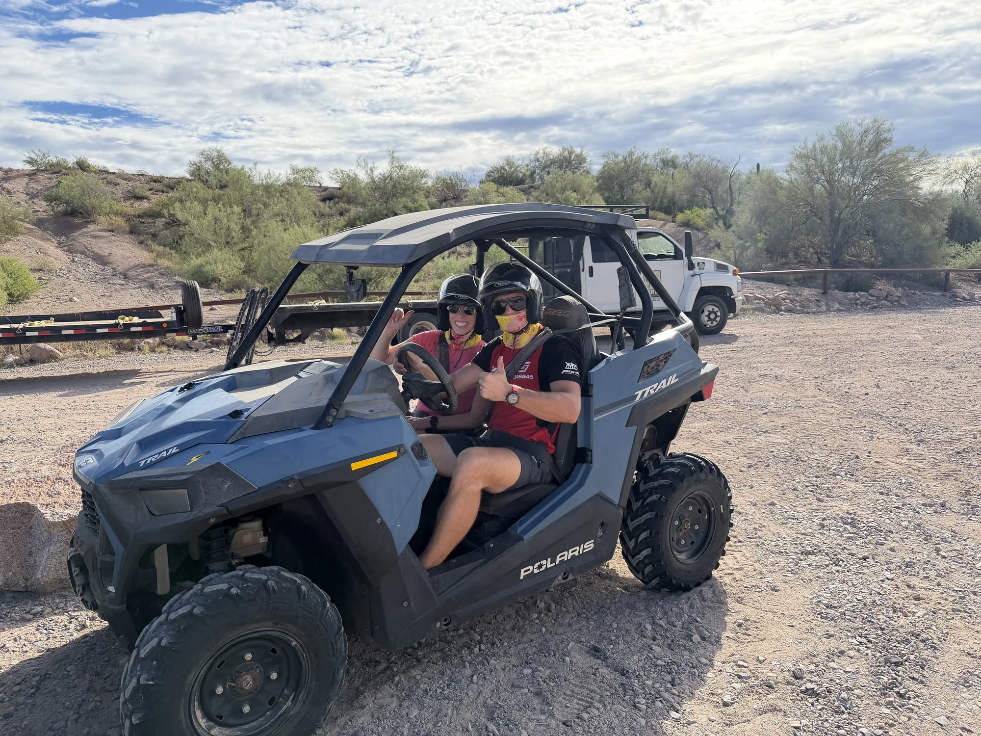 A couple in helmets giving a thumbs up from the cockpit of a Polaris RZR before a Scottsdale desert tour