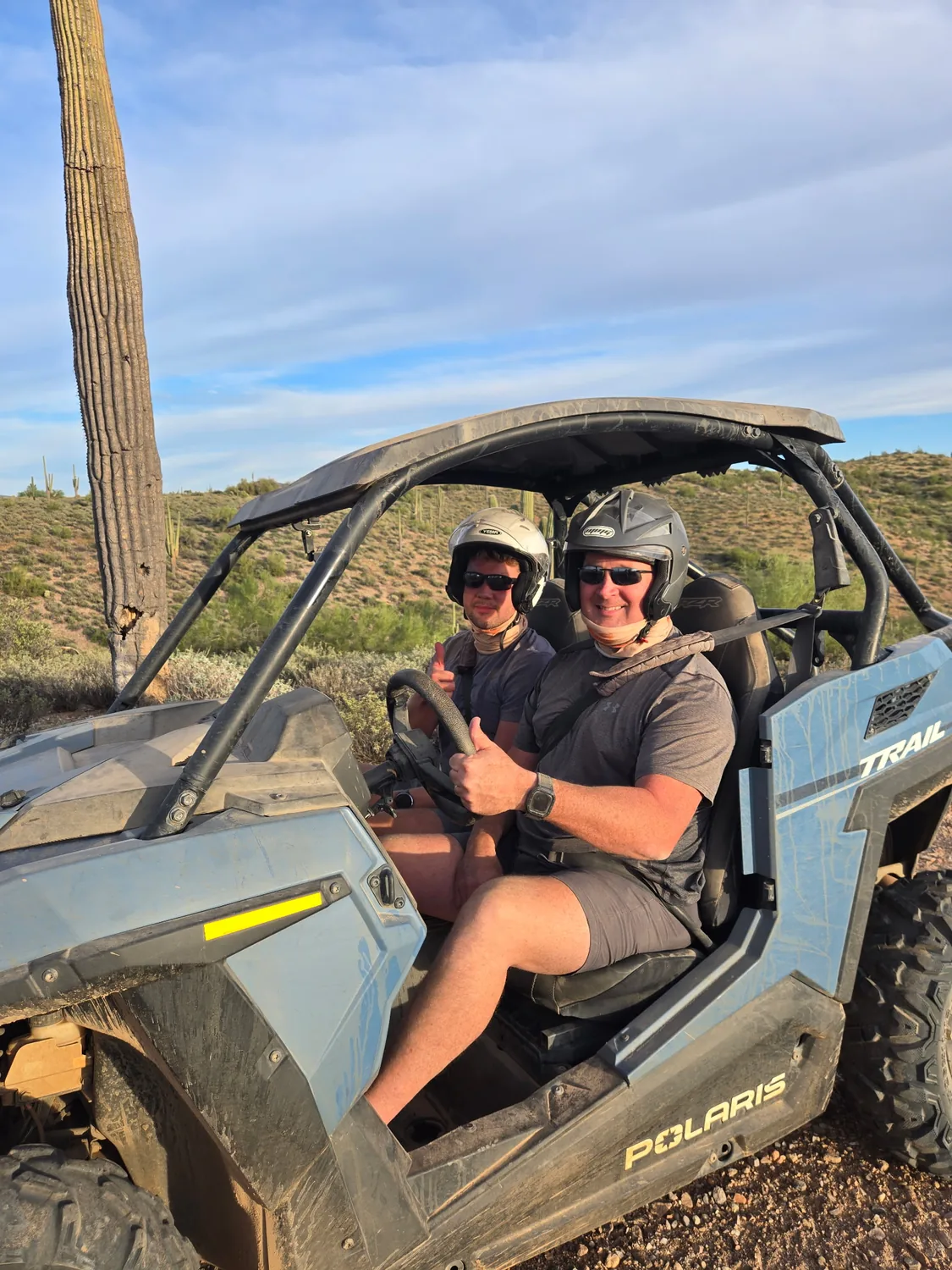 A couple giving a thumbs up from their RZR at golden hour beside a saguaro near Scottsdale