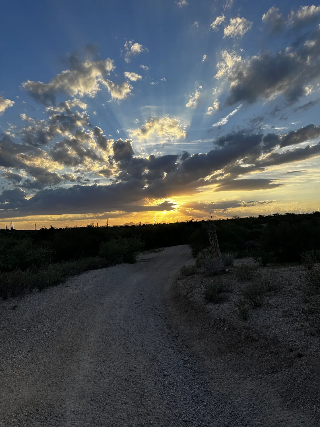 Sun rays bursting through the clouds over a desert dirt road at sunset near Scottsdale