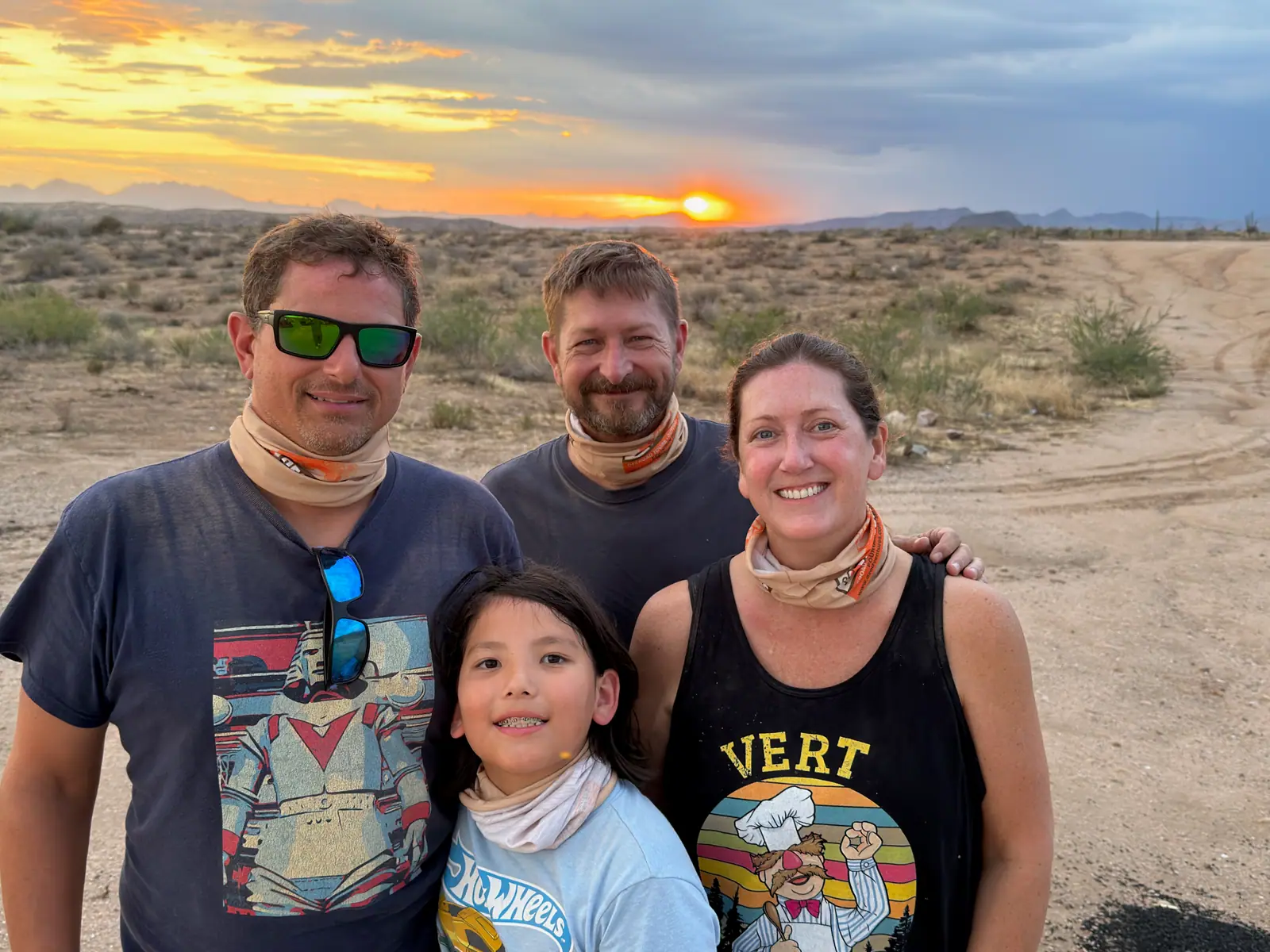 A family in Desert Dog neck gaiters taking a selfie at a vivid desert sunset near Scottsdale