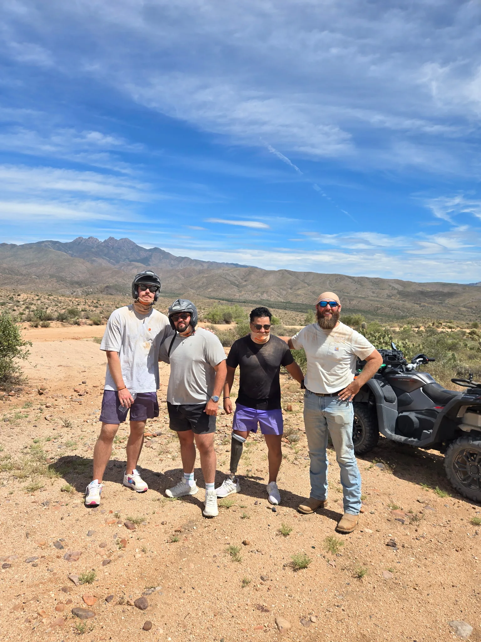 Four friends with an ATV under a blue sky with the Four Peaks behind them on a Scottsdale desert tour