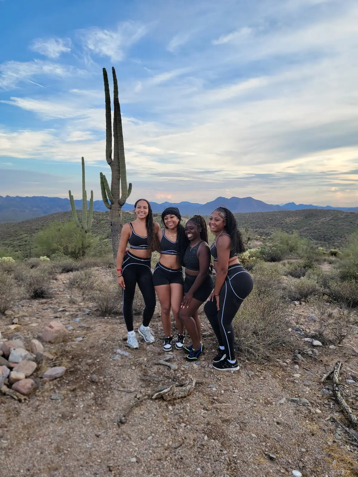 A group of friends posing by a tall saguaro cactus at sunset on a Scottsdale UTV tour