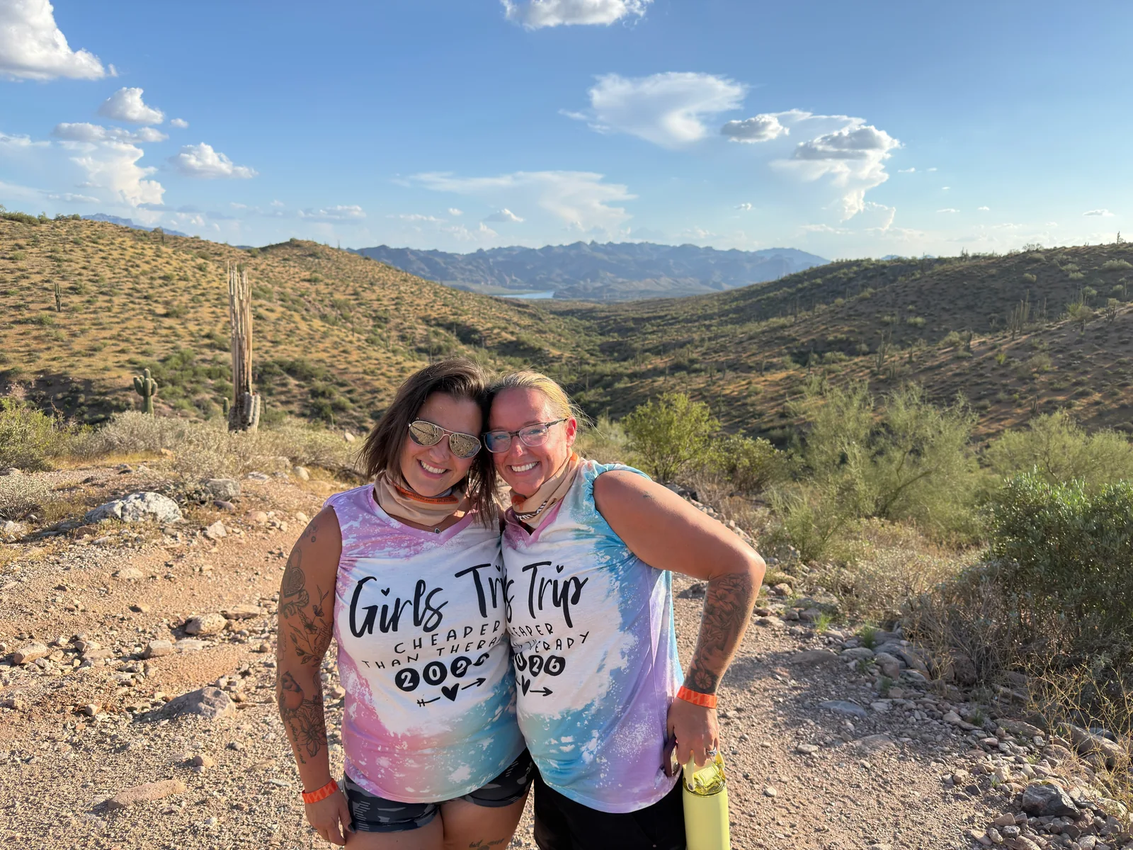 Two friends on a girls trip hugging at a golden-hour desert valley overlook near Scottsdale