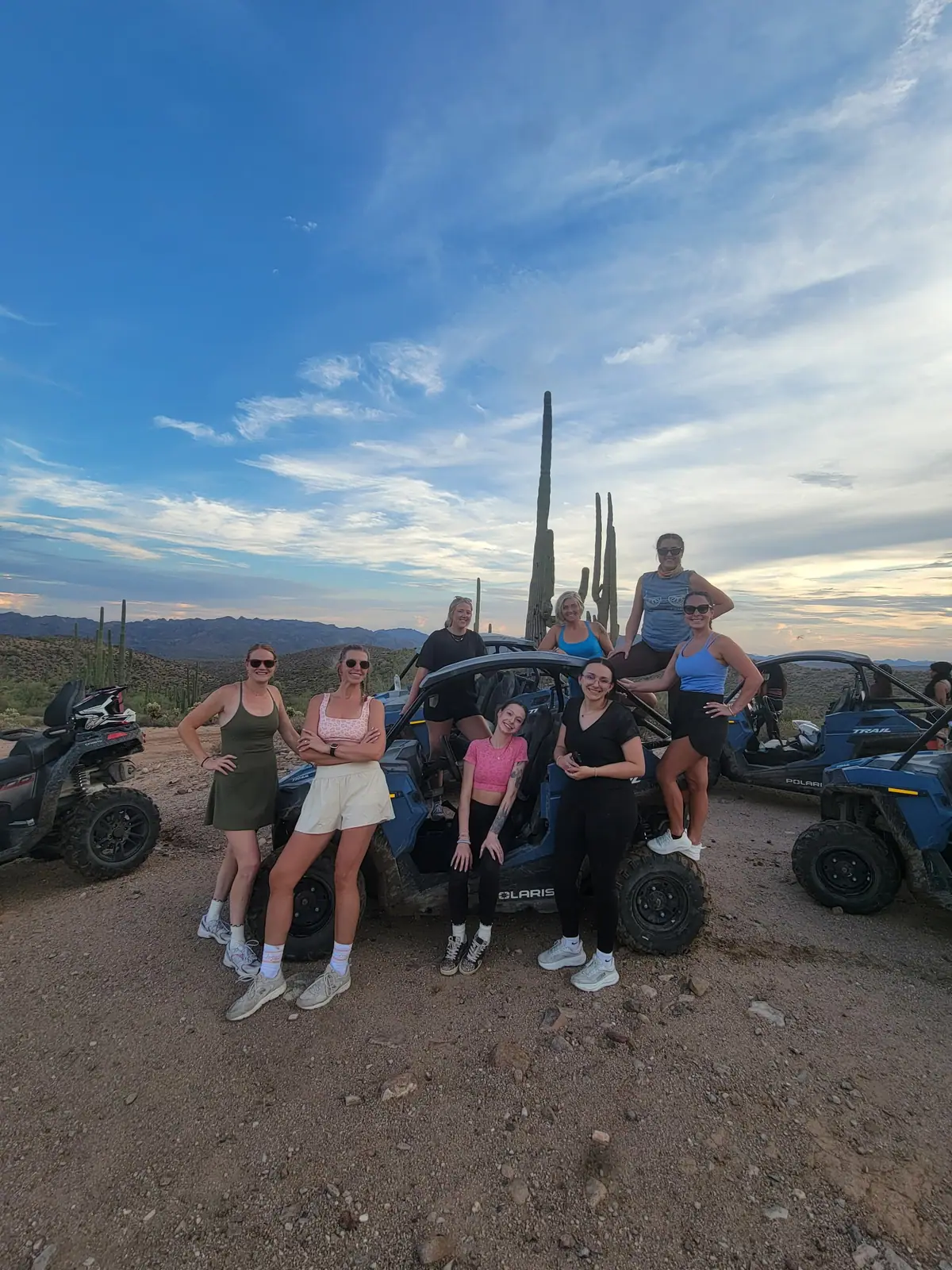 A tour group gathered around a blue Polaris RZR among saguaros at sunset near Scottsdale
