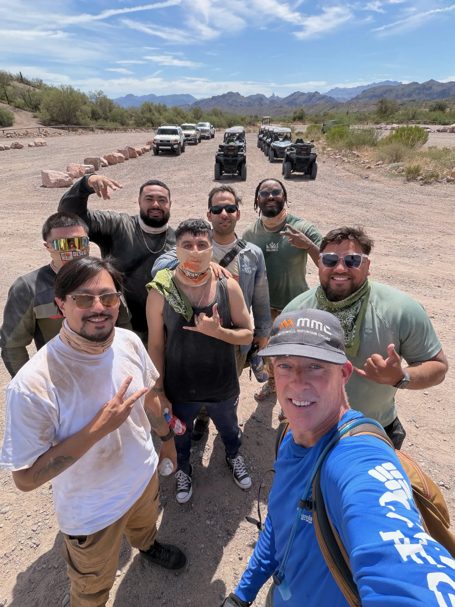 A Desert Dog Offroad Adventures guide and tour group in a trailside selfie with the UTV convoy lined up behind them near Scottsdale