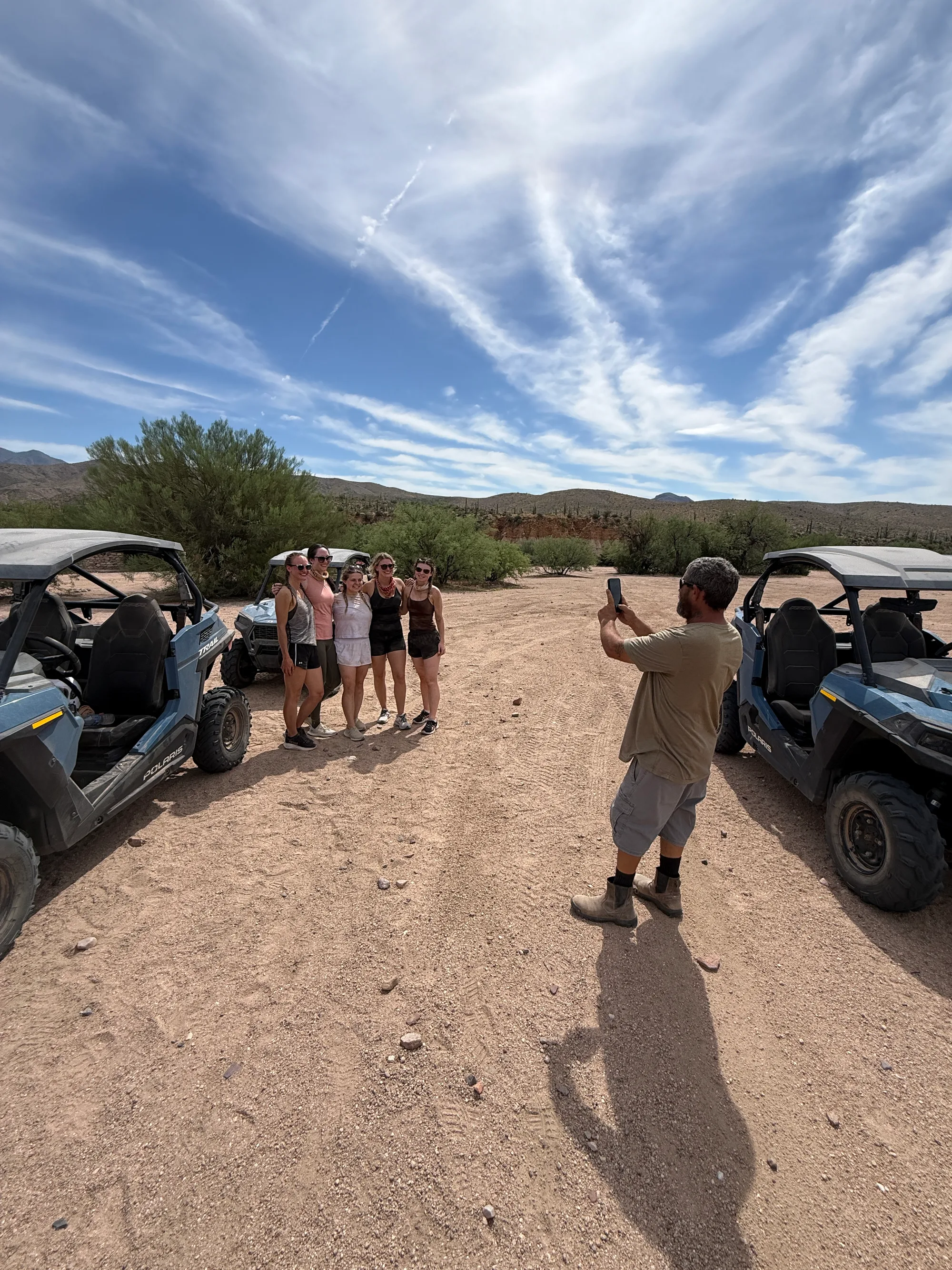 A Desert Dog Offroad Adventures guide taking free tour photos of a bachelorette group between two Polaris RZRs