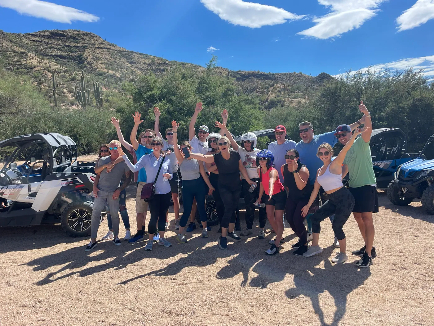 A large group cheering with arms raised beside their buggies in the Scottsdale desert