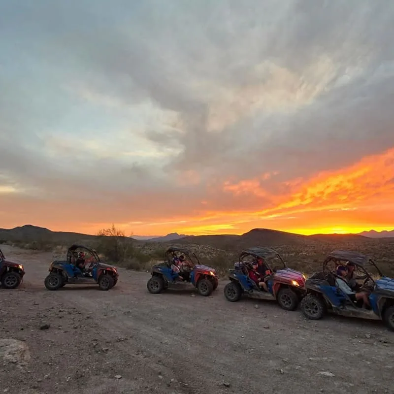 Sand buggies lined up on a desert trail at vibrant sunset