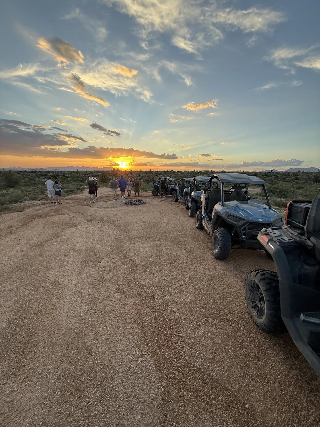 A lineup of sand buggies beside a group gathered around a firepit watching the Sonoran Desert sunset near Scottsdale