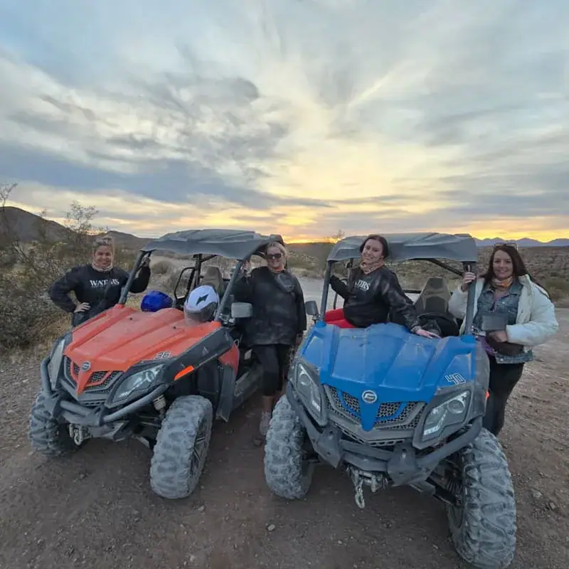 Four people beside orange and blue buggies at sunset