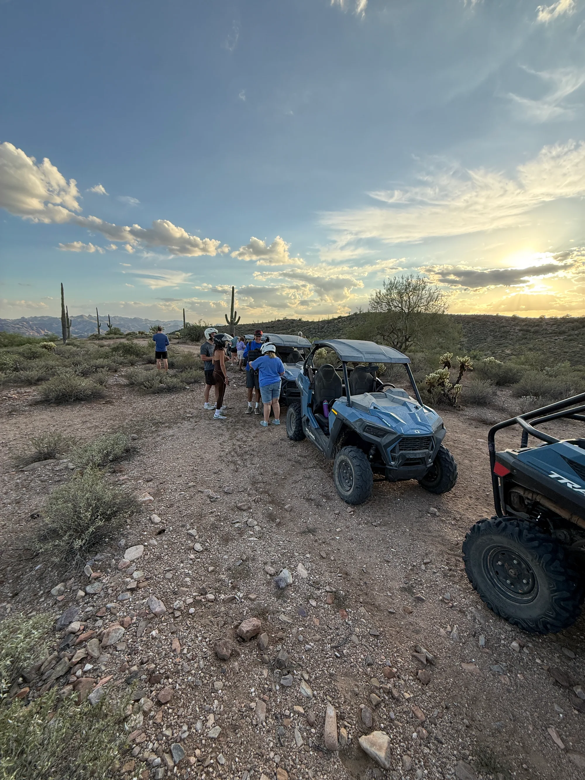 A tour group gathered by their Polaris RZRs on a saguaro ridge as the sun bursts through the clouds near Scottsdale
