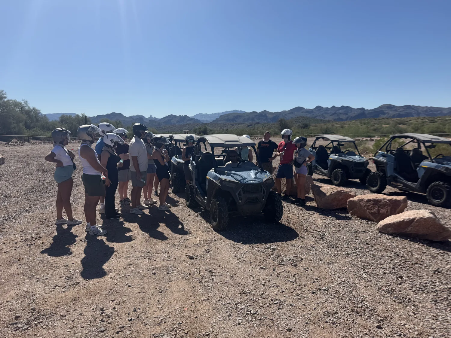 A tour group gathered by the RZR fleet at the staging area with the mountains behind near Scottsdale