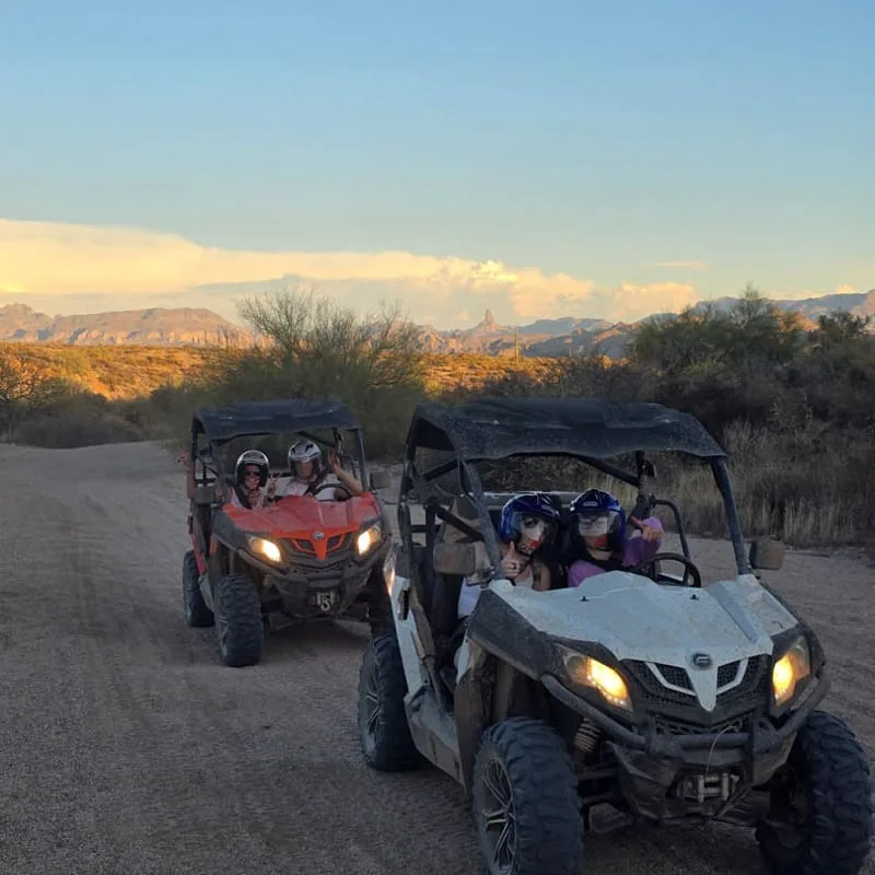 Two sand buggies driving a scenic desert trail at sunset