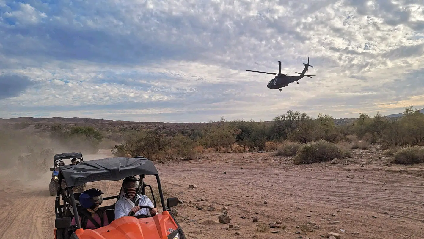 A UTV on the trail as a Black Hawk helicopter flies over the Sonoran Desert